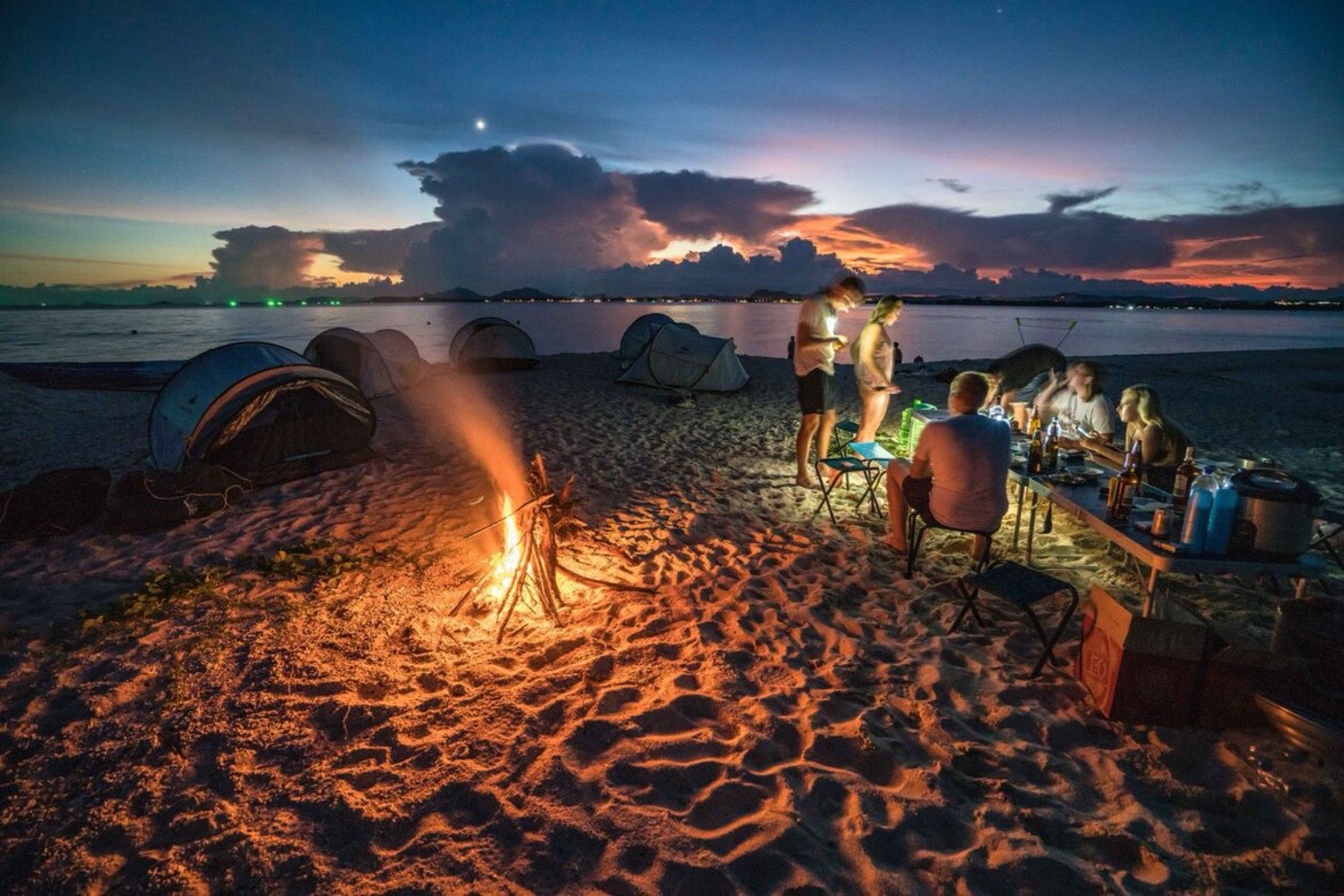 The group sharing a seafood BBQ around the campfire on the beach at dusk
