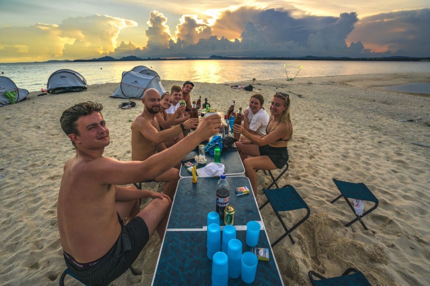The group raising a toast around the table on the beach at sunset