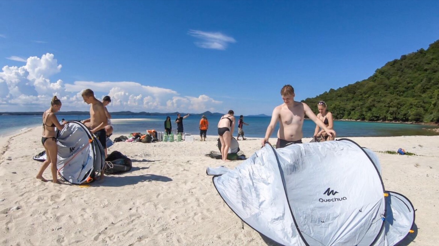 The group pitching tents on the bright white beach under a blue sky