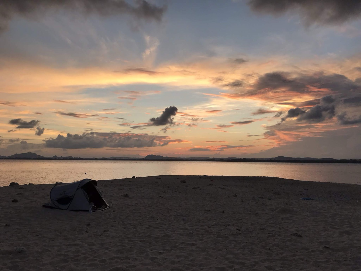 A single tent on the sand spit beneath a dramatic painted sunset sky
